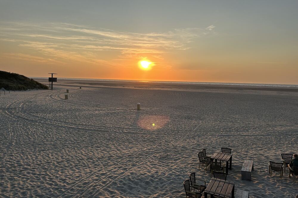 Zonsondergang boven zee op het brede strand van Ouddorp, met houten stoelen en tafels op het zand
